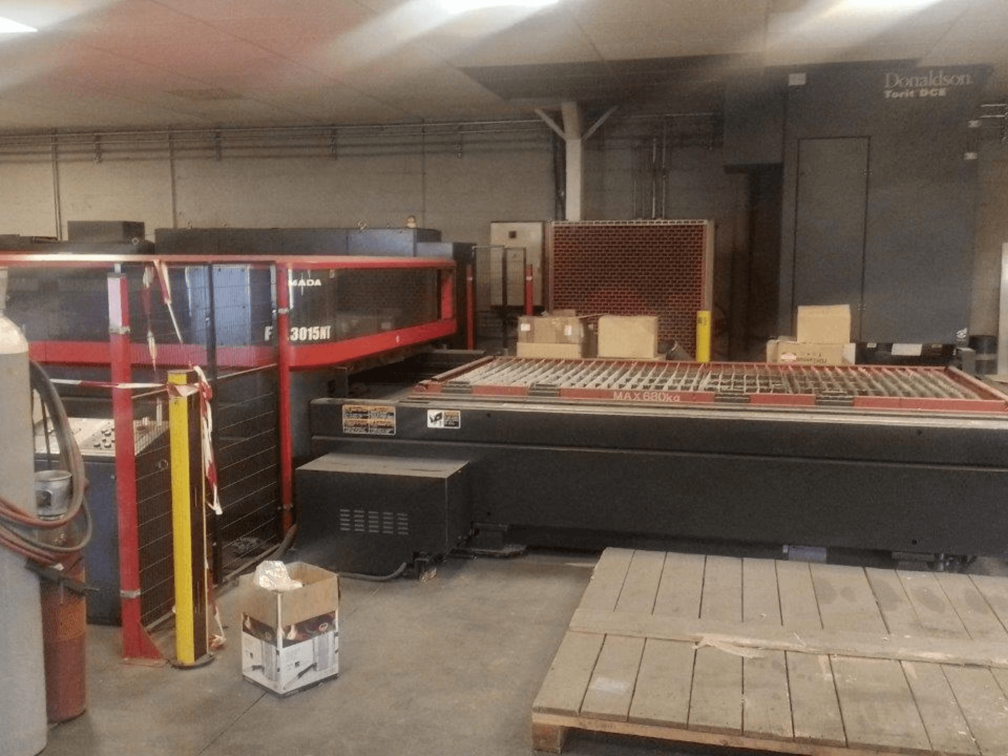 AMADA FOL 3015 NT CO2 laser cutting machine, front view; red safety enclosure, work table with grid, industrial setting.
