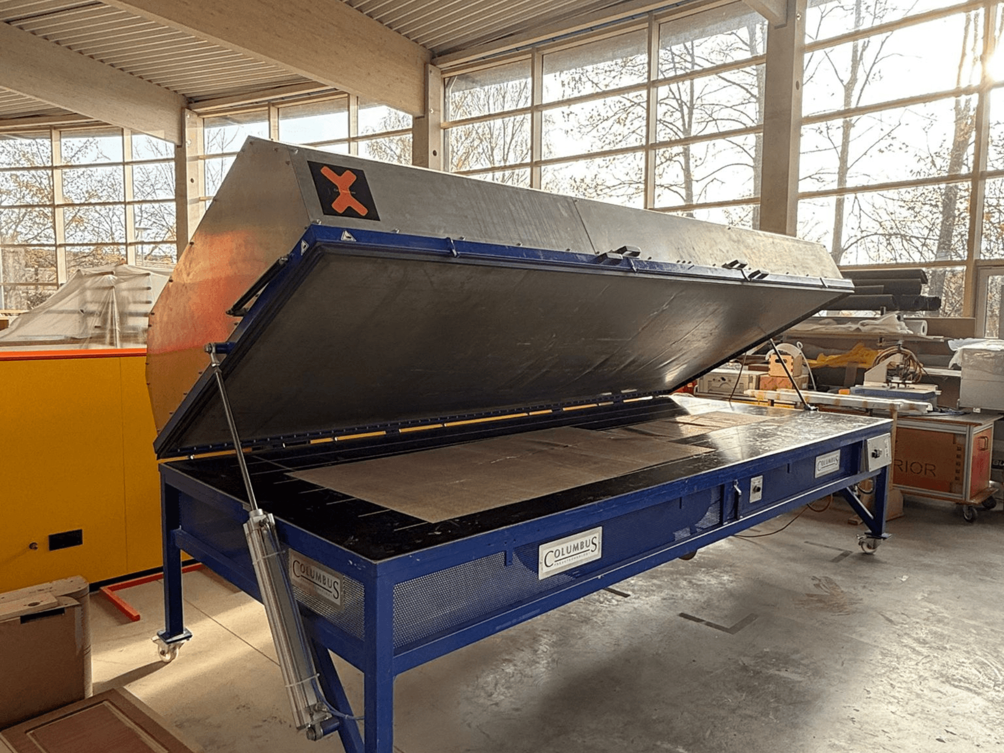 Columbus vacuum press in a workshop, front view with large angled top open, showcasing a flat surface and detailed machinery.