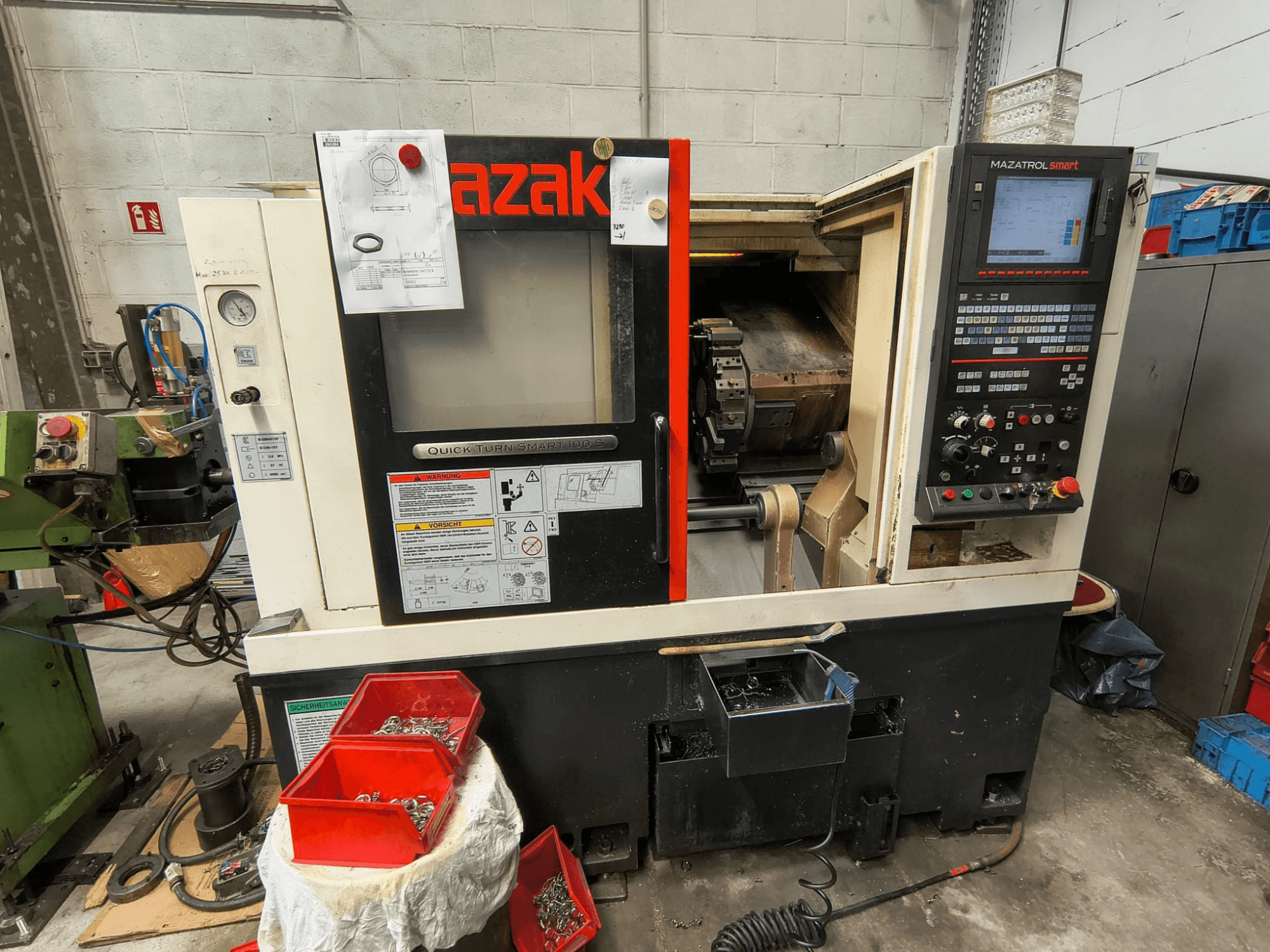 Mazak Quick Turn Smart 100 S, side view showing control panel, coolant tray, and storage bins with screws.