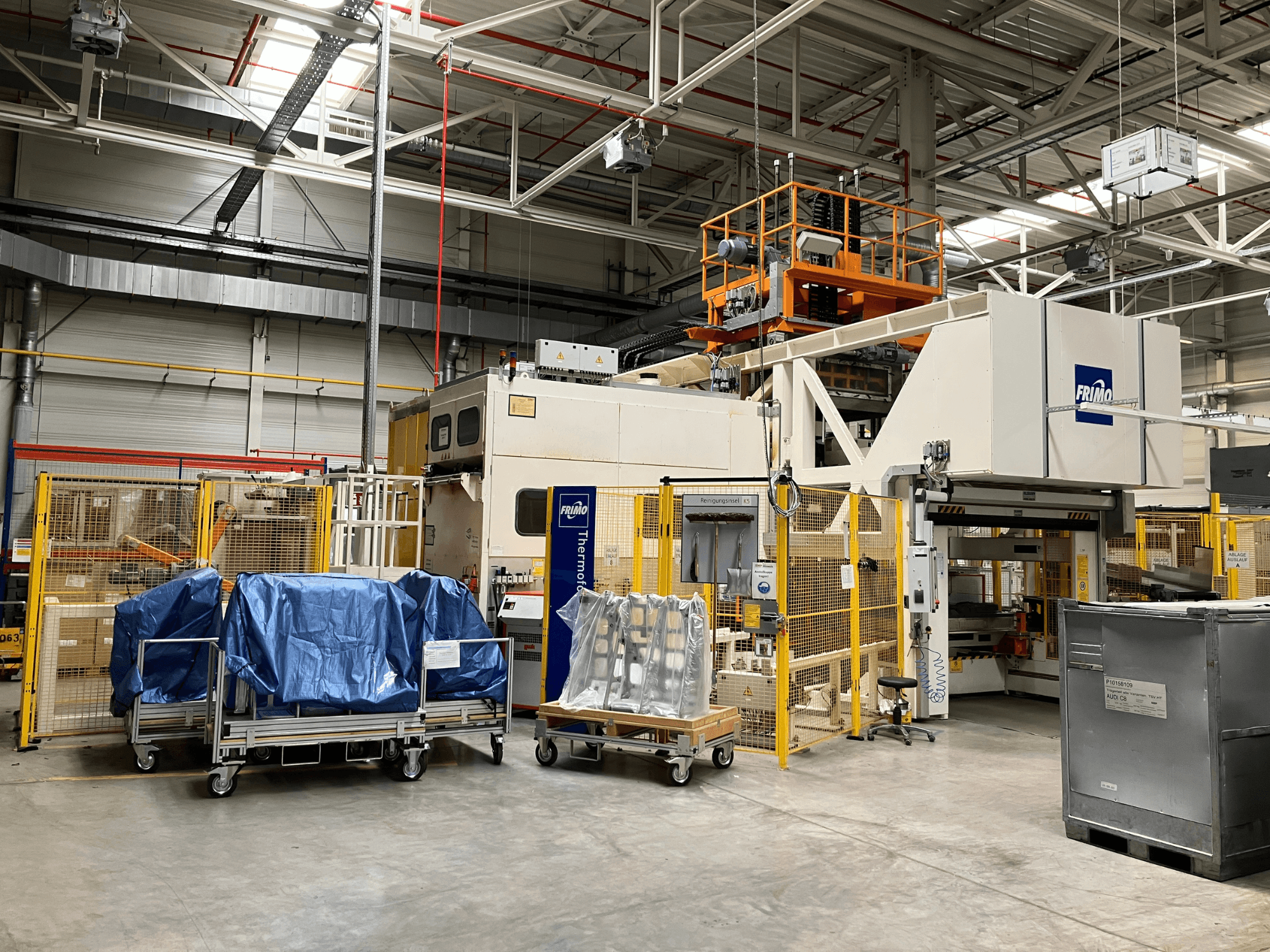 FRIMO FTL 80/200 Fullflex plastic processing machine in a factory, front view with blue tarps and safety barriers visible.
