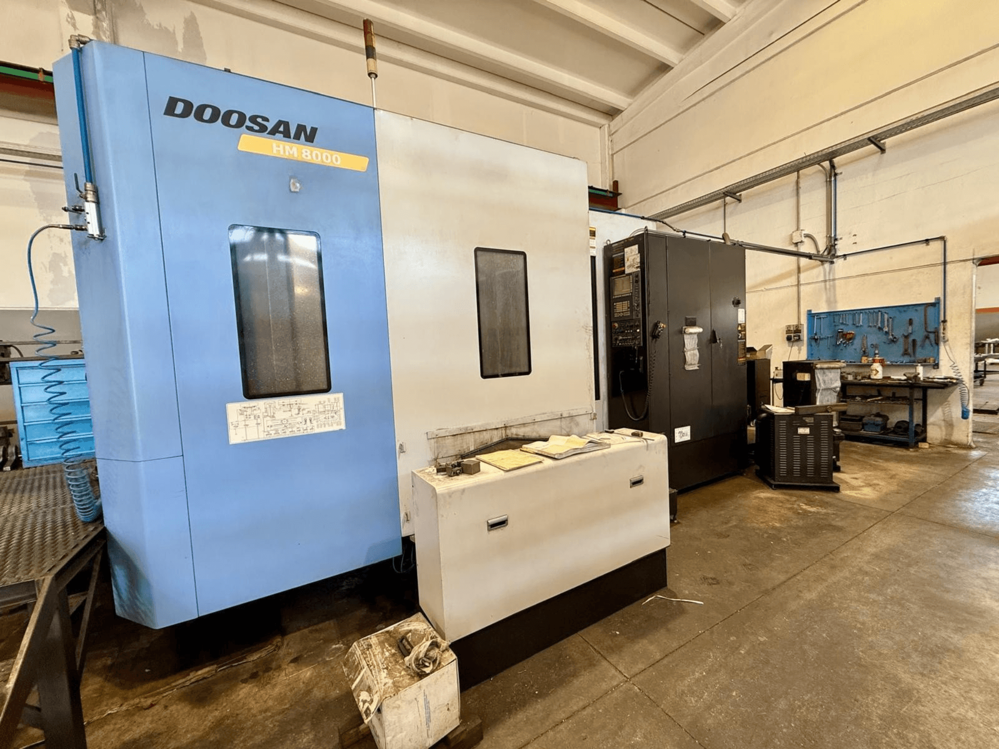 DOOSAN HM 8000 horizontal machining center in blue, front view, showing control panel and nearby workshop equipment.