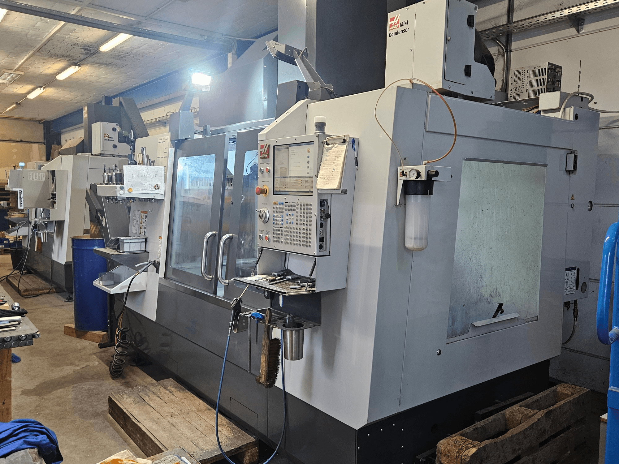 Haas VF-3YT/50 vertical machining center in a workshop, front view showing control panel, tool holders, and mist condenser.