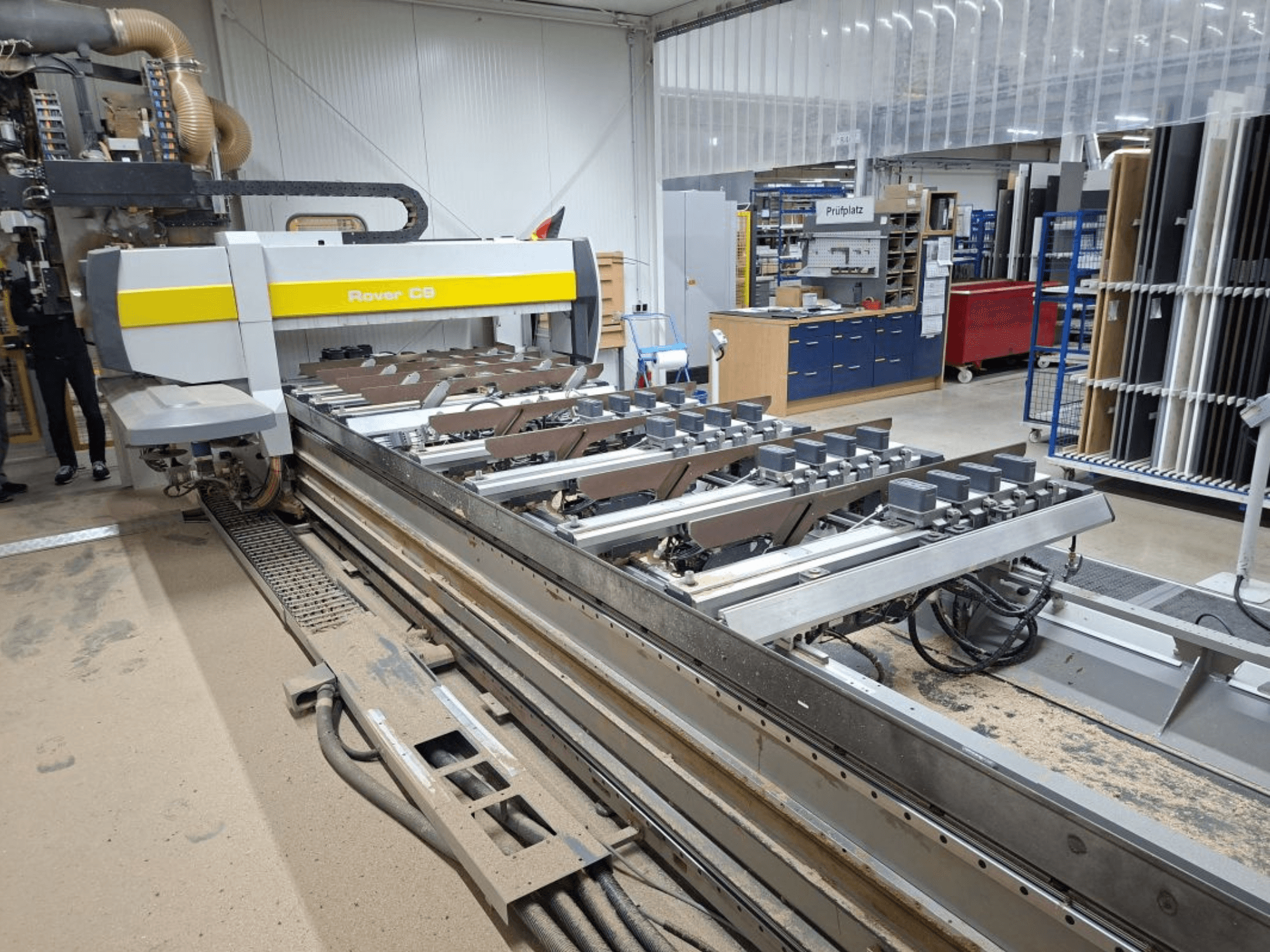 Rover C9 CNC machine in a workshop; front view shows cutting tools and conveyor system, with dust accumulation on the floor.