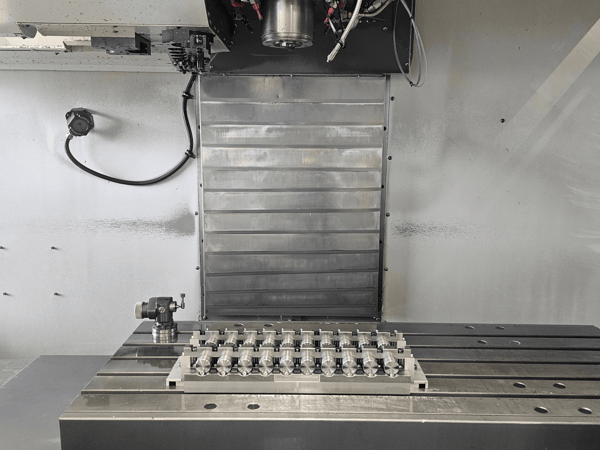 Front view of a CNC milling machine's workspace featuring a precision machined part on metal table and control mechanisms.