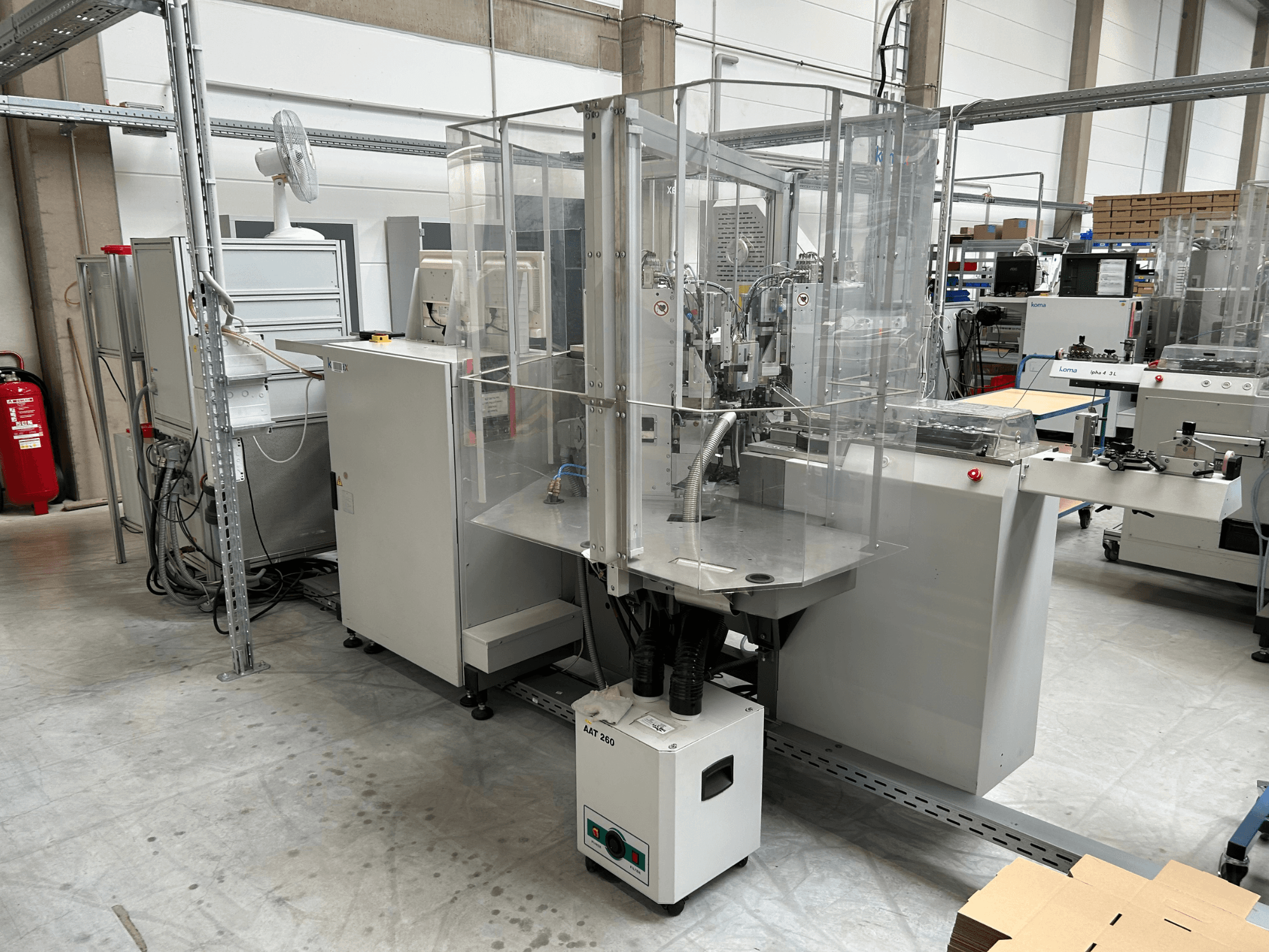 KOMAX Alpha 433 L automation equipment in a factory setting. Features transparent safety enclosure and various control panels.