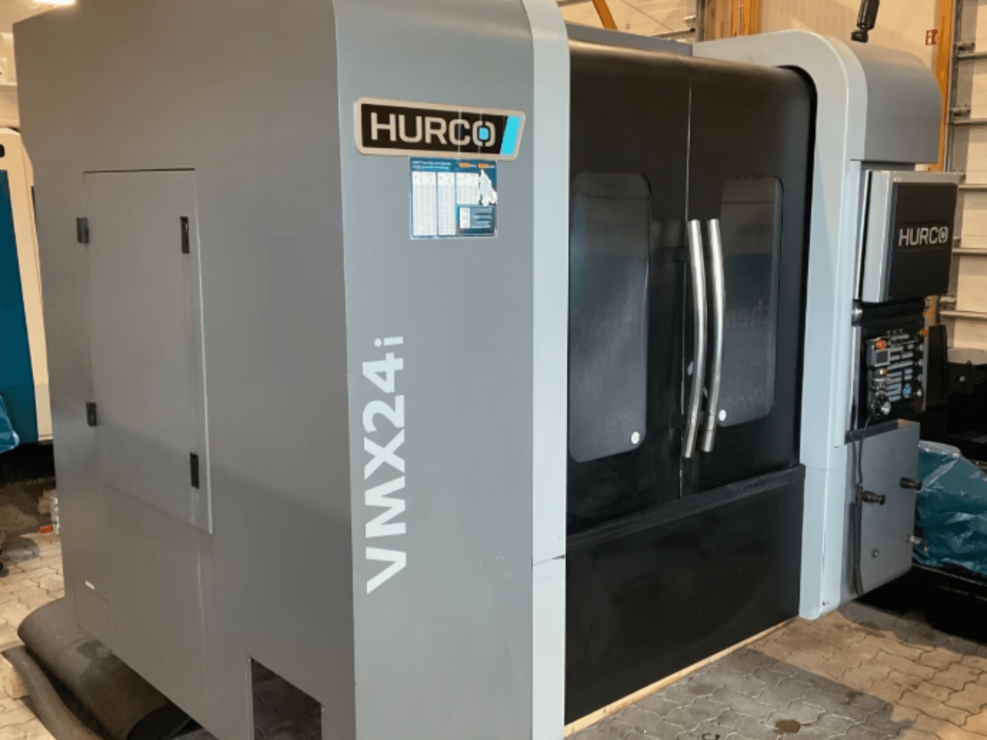 Hurco VMX 24i vertical machining center, front view with a metallic gray body, black panel doors, and control interface.