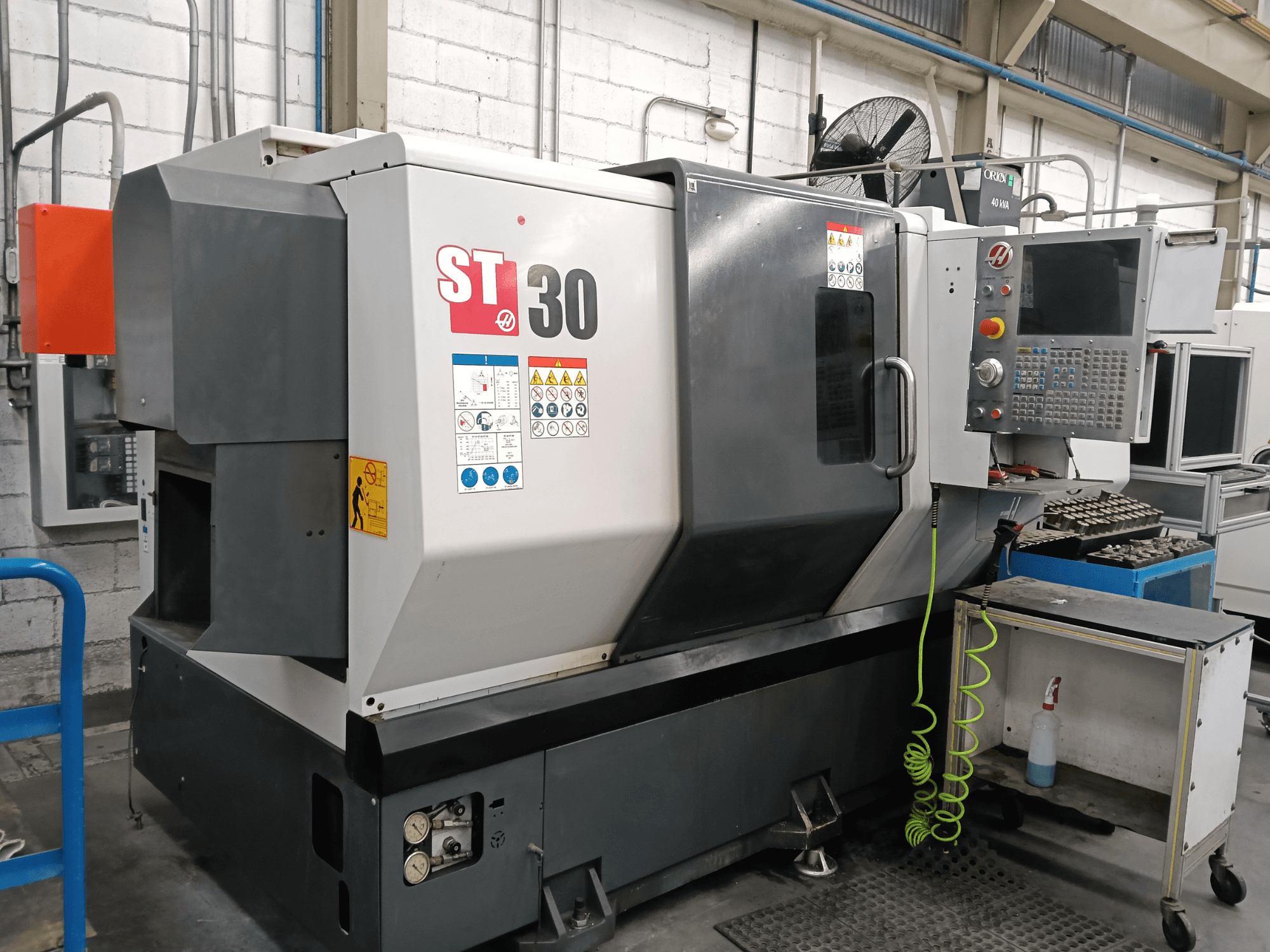 Alt text: Front view of HAAS ST-30 horizontal turning machine with control panel, safety labels, and tools on a nearby cart.