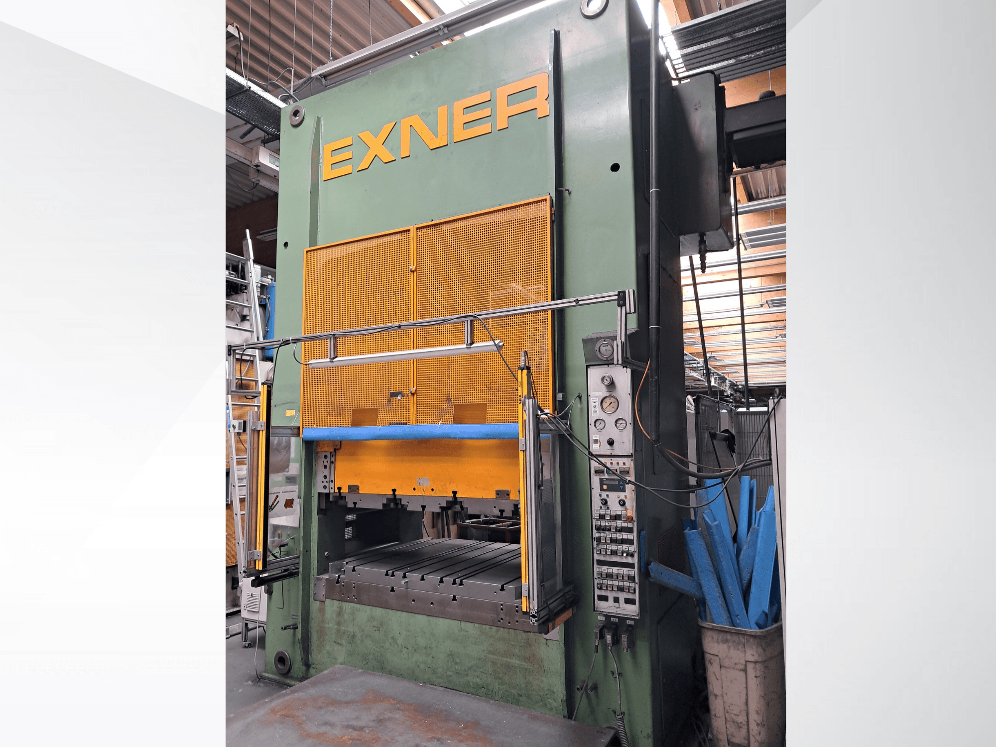 Hydraulic press EXNER EX SBR 150, front view; featuring controls, blue safety bar, and mesh guard, set in a workshop environment.