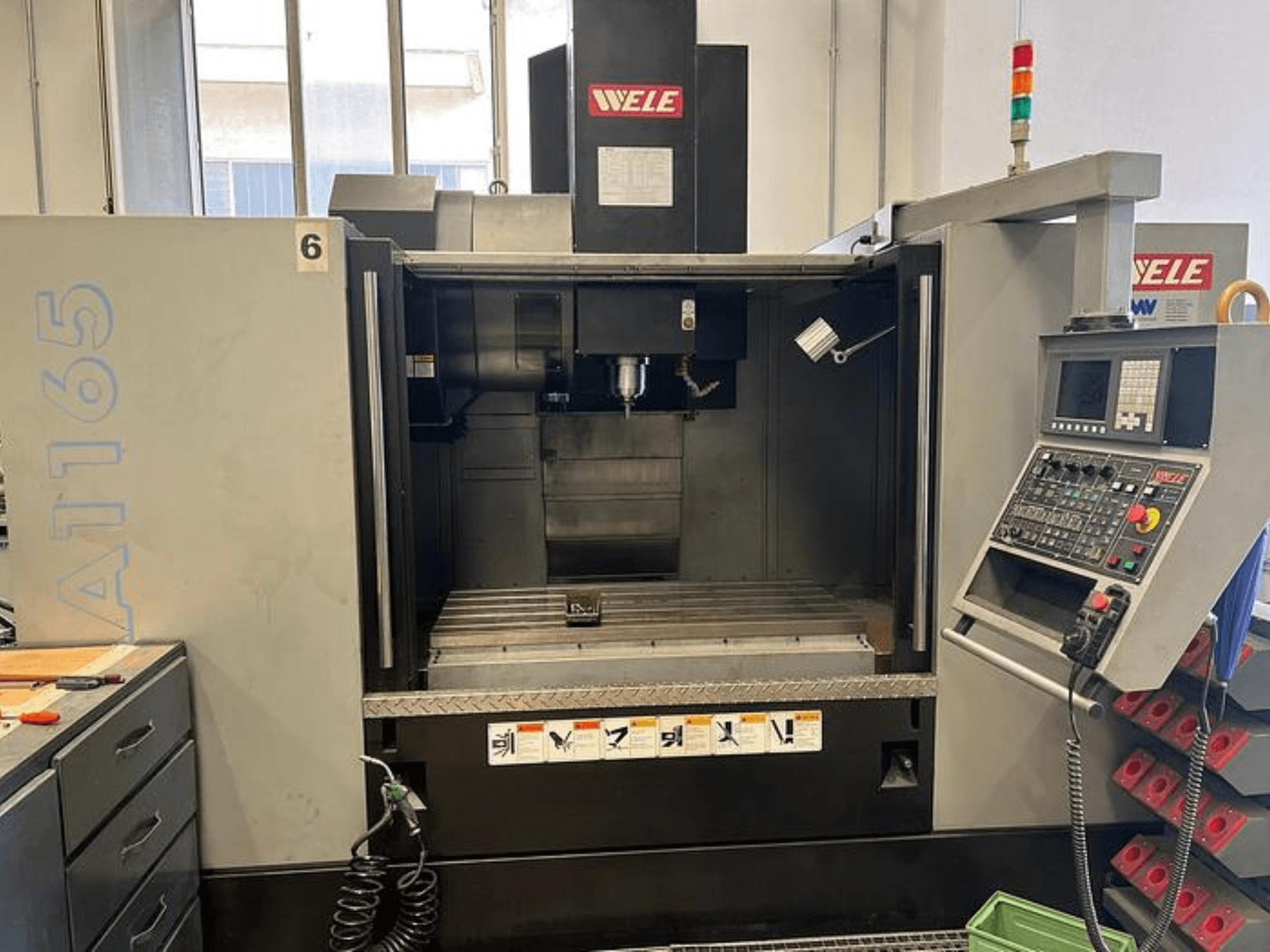 WELE A165 CNC machining center, front view, with control panel, tool holder, and worktable visible. Industrial setting.