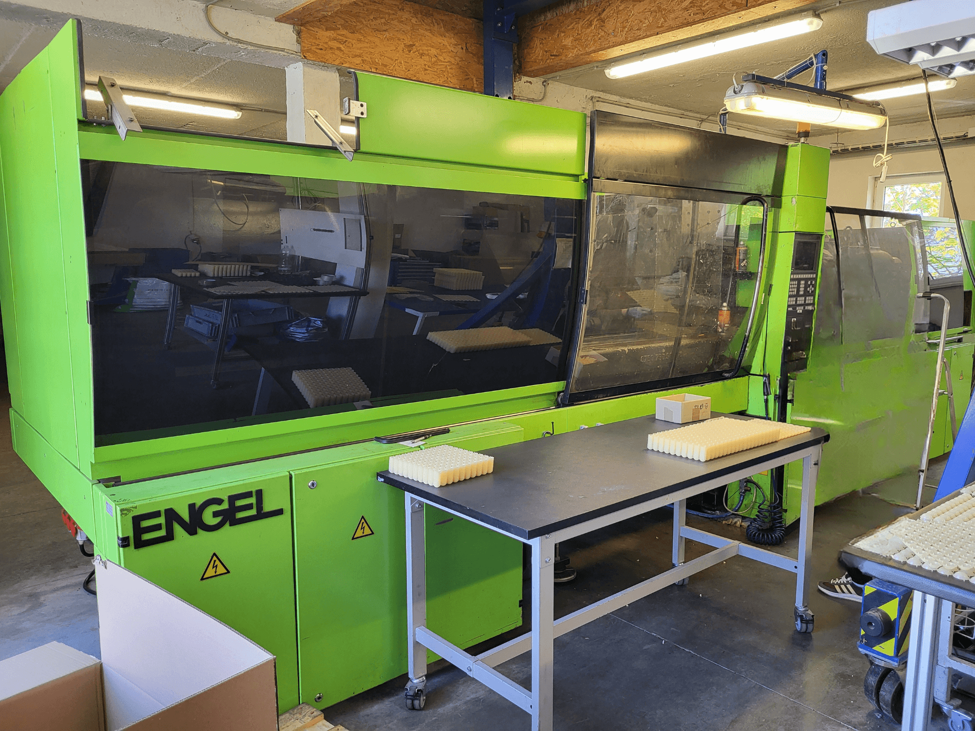 Green Engel ES1800/300HL hydraulic injection moulding machine viewed from the front, with stacked materials on a worktable.