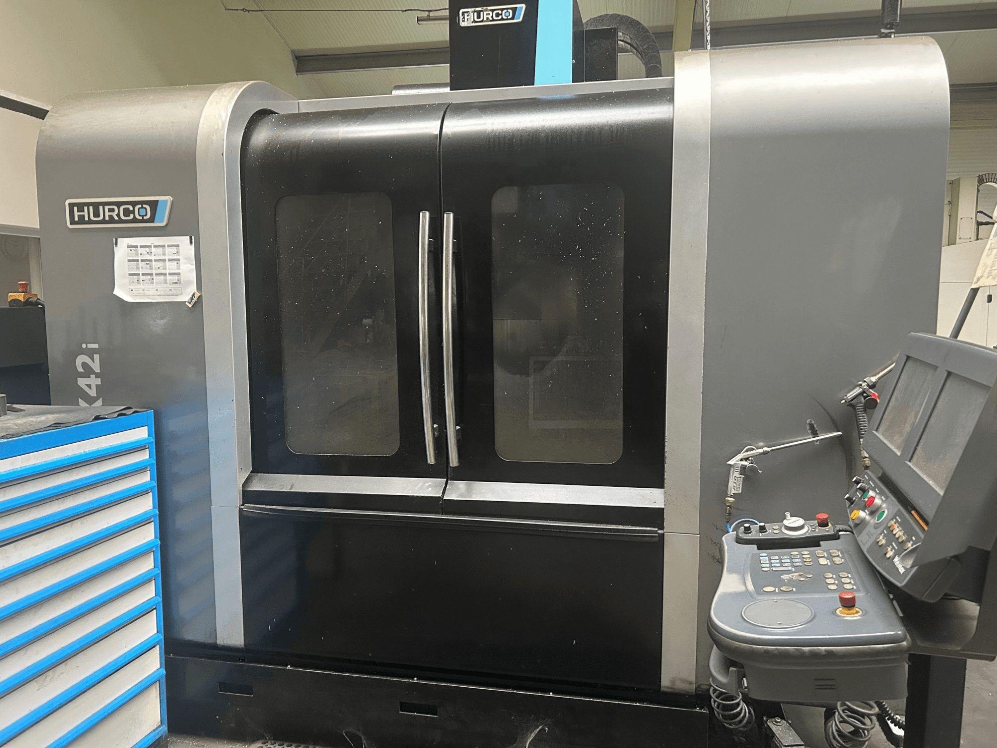 Hurco VMX42i CNC machine, front view with control panel on the side, features double doors and visible technical details.