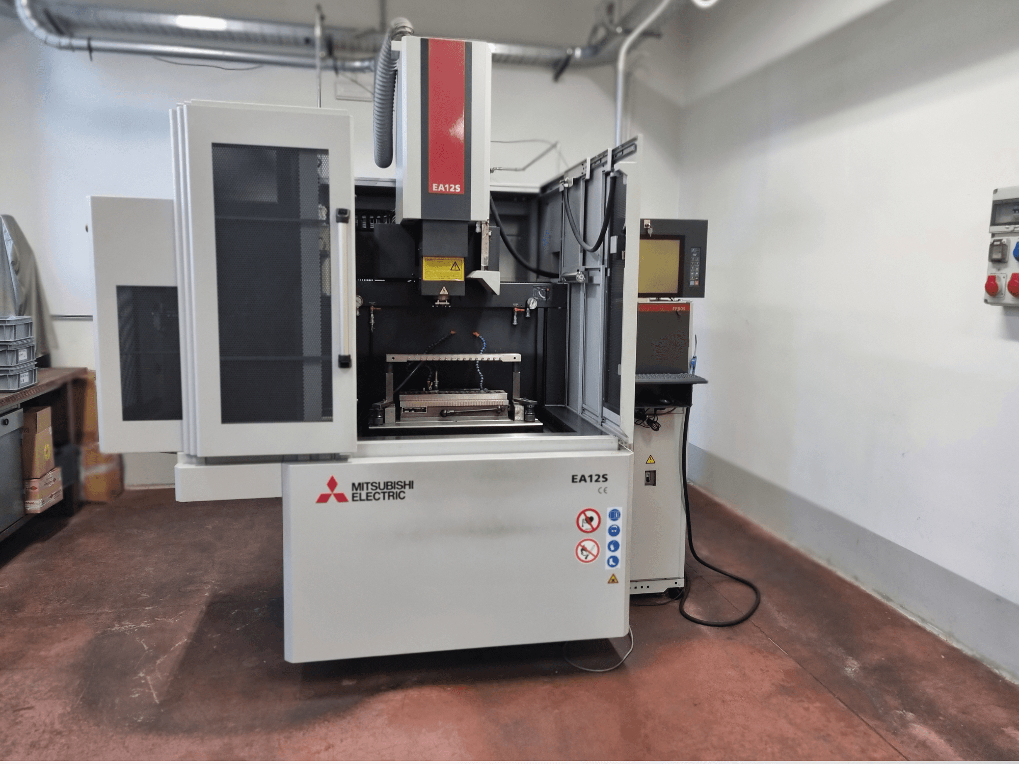 Mitsubishi Electric EA12S wire cutting machine, front view, features open doors, control panel, and safety labels.