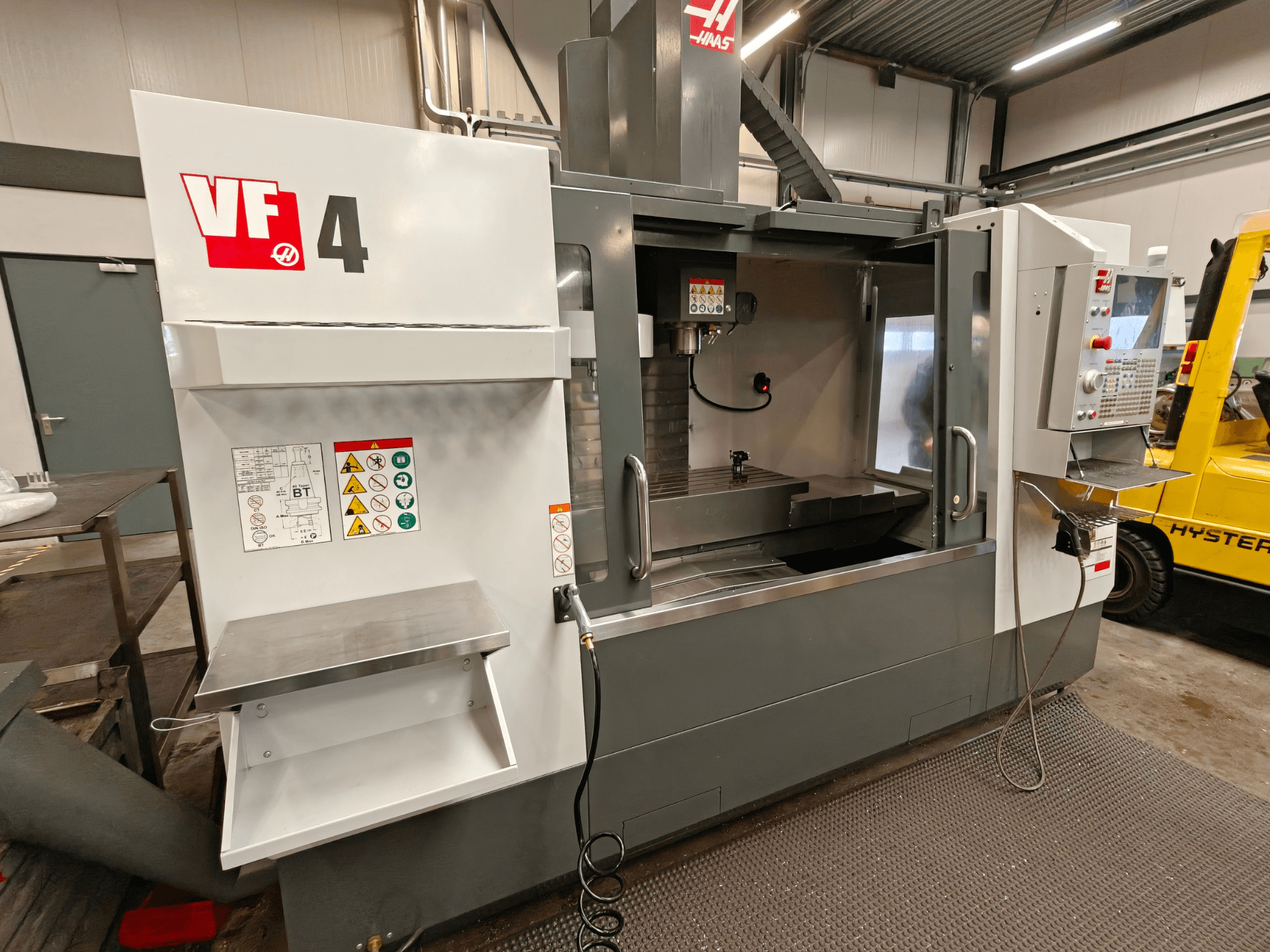 HAAS VF-4 vertical machining center, front view, featuring control panel, work area, and safety labels on the side.