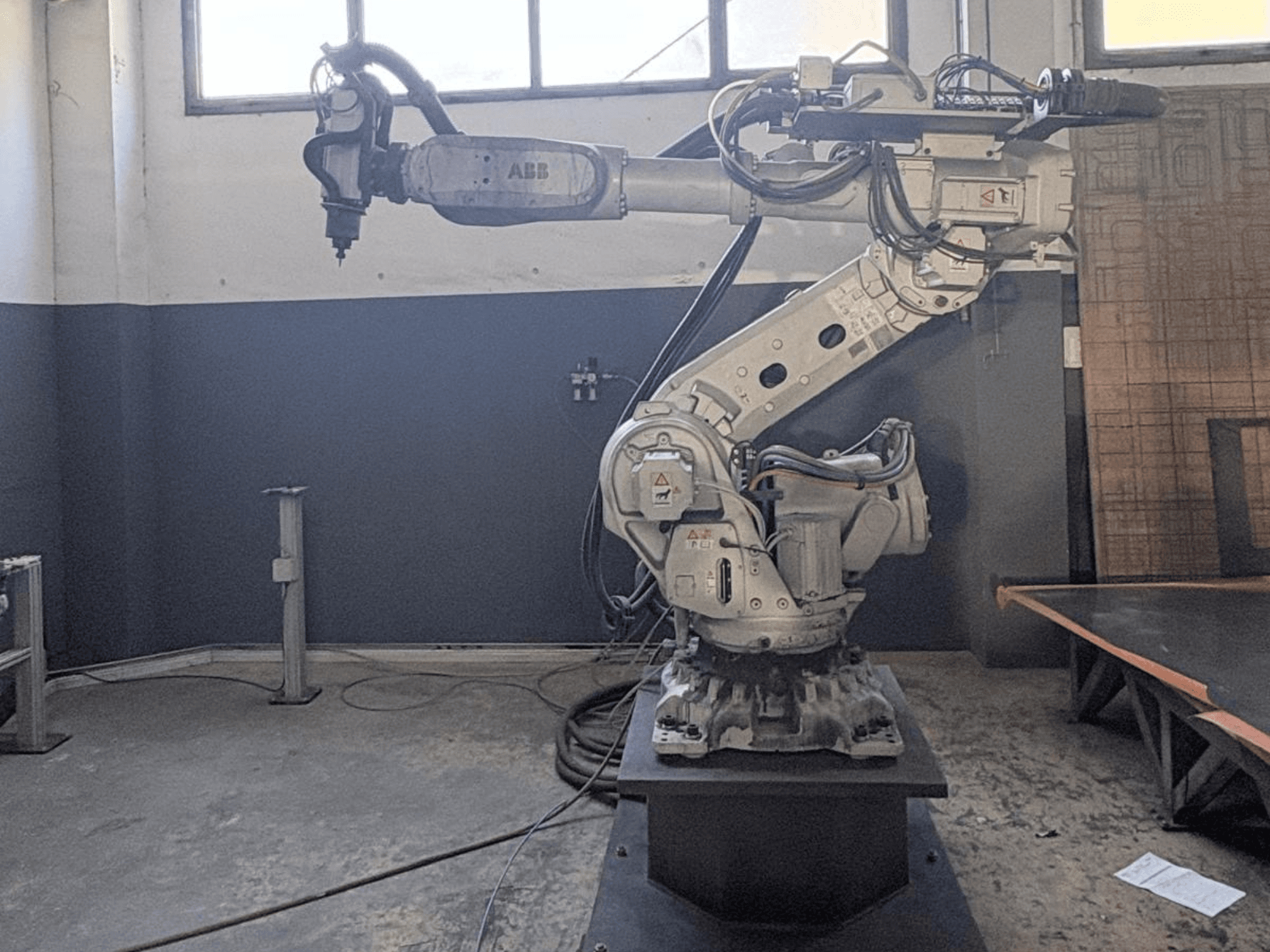 ABB IRB 6700 robot arm in a front view, showcasing its joints, cables, and mounted base in a workshop setting.